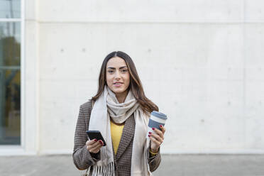 Young woman with smart phone and reusable coffee cup on footpath - EIF03172