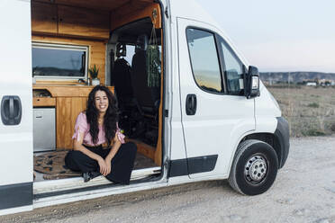 Glückliche junge Frau sitzt in einem auf einem Feldweg geparkten Lieferwagen - EGHF00331