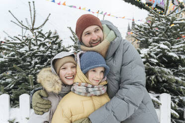 Smiling father embracing children at backyard in winter - EYAF01870