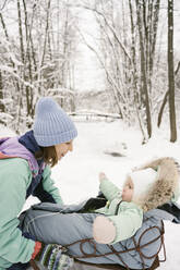 Smiling woman looking at daughter on sled in winter - EYAF01874