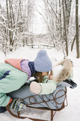 Mother playing with daughter on sled in winter - EYAF01875