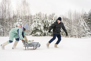 Glücklicher Vater und glückliche Mutter schlittern mit ihrer Tochter durch den Schnee im Winter - EYAF01880