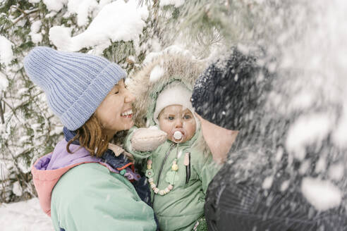 Frau trägt ihre Tochter zu einem Mann, der im Winter mit Schnee spielt - EYAF01887