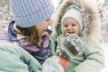 Junge Frau in warmer Kleidung spielt mit ihrer süßen Tochter im Winter - EYAF01890