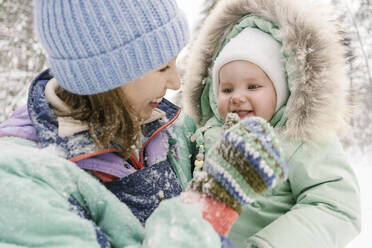 Young woman in warm clothing playing with cute daughter in winter - EYAF01890