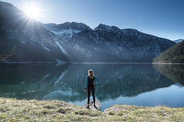 Frau mit Hand an der Hüfte blickt über den Plansee auf die Ammergauer Alpen, Reutte, Tirol, Österreich - WFF00609