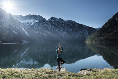 Frau übt Yoga in der Baumhaltung am Plansee, Ammergauer Alpen, Reutte, Tirol, Österreich - WFF00610