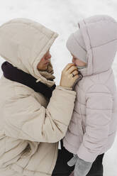 Mother helping daughter getting dressed in winter - SEAF00396