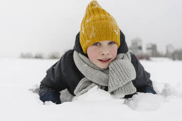 Junge mit gelber Strickmütze auf Schnee liegend - SEAF00401