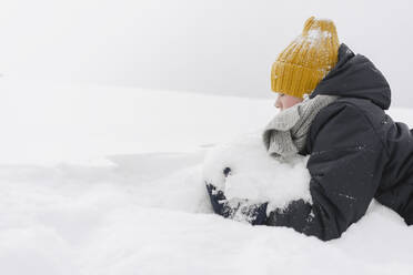 Junge mit gelber Strickmütze spielt mit Schnee - SEAF00404