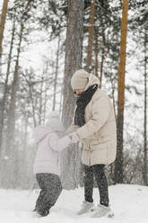 Daughter playing with mother in snowy forest - SEAF00409