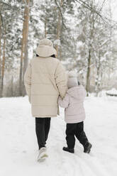 Mother and daughter walking together on snow in winter forest - SEAF00412