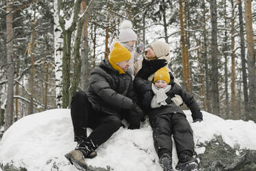 Mann und Frau sitzen mit Tochter und Sohn im Schnee im Winterwald - SEAF00415
