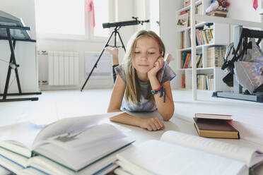 Girl looking at books lying on floor at home - EYAF01899