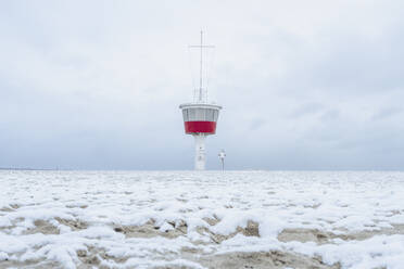Germany, Schleswig-Holstein, Lubeck, Snow covered beach in Travemunde with lookout tower in background - KEBF02192