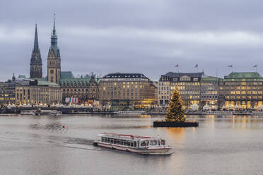 Germany, Hamburg, Tourboat sailing across Inner Alster Lake with Christmas tree and city buildings in background - KEBF02202