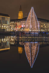 Germany, Schleswig-Holstein, Kiel, Large Christmas tree reflecting in city canal at night - KEBF02204