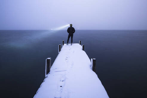 Tourist mit Stirnlampe bewundert See stehend auf Steg im Winter, Walchensee, Bayern, Deutschland - WFF00635