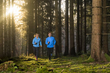 Mann und Frau joggen im Wald bei Sonnenuntergang - STSF03129