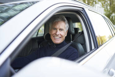 Smiling elderly man sitting in car on road trip - PNEF02617