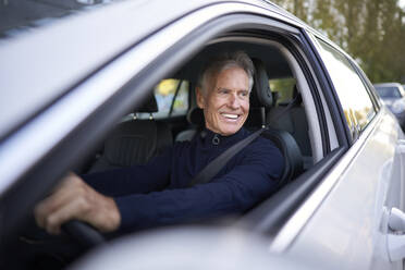 Smiling senior man driving car - PNEF02629