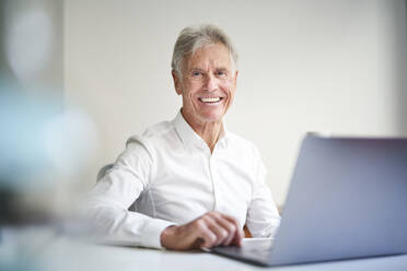 Lächelnder Geschäftsmann mit Laptop am Schreibtisch im Studio - PNEF02652