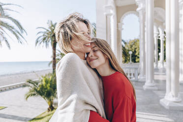 Smiling teenage girl with eyes closed embracing mother on sunny day - OMIF00481