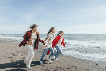 Friends running on sand at seashore - OMIF00487