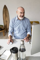 Smiling senior businessman using computer at desk in home office - GIOF14759