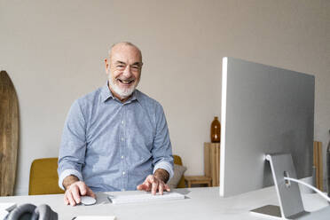 Happy senior freelancer with computer sitting at desk - GIOF14761