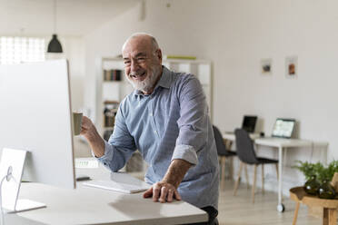Happy businessman with computer sitting at desk - GIOF14774