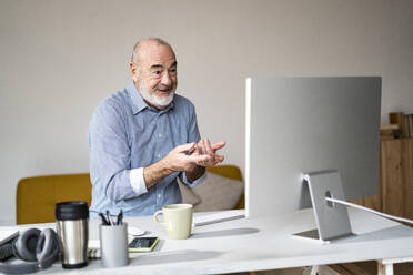 Freelancer gesturing on video call through desktop computer at desk - GIOF14775