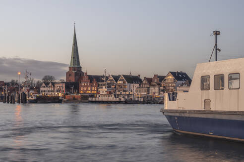 Deutschland, Schleswig-Holstein, Lübeck, Skyline von Travemünde in der Abenddämmerung mit Fähre im Vordergrund - KEBF02223