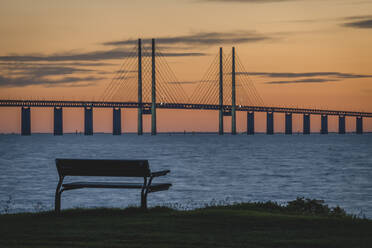 Sweden, Skane County, Malmo, Oresund Bridge at dusk with empty park bench in foreground - KEBF02232