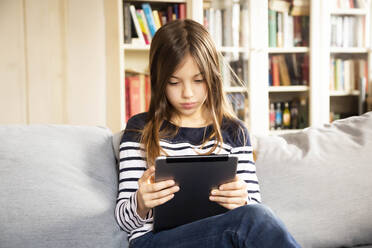 Young girl sitting on living room sofa with digital tablet in hands - LVF09188