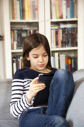 Junges Mädchen sitzt auf dem Wohnzimmersofa mit digitalem Tablet in den Händen - LVF09189