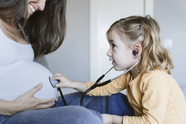 Curious girl listening to pregnant mother's belly through stethoscope - EBBF05231