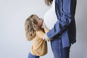 Nettes blondes Mädchen küsst den Bauch der schwangeren Mutter an der Wand - EBBF05245