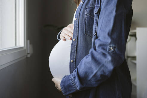 Schwangere Frau berührt Bauch am Fenster zu Hause - EBBF05255