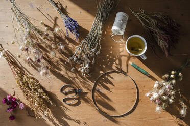 Studioaufnahme von Schere, Draht, Faden und verschiedenen getrockneten Blumen, die zu einem Kranz geflochten werden sollen - EVGF03970