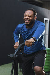 Lächelnder Sportler beim Training auf dem Airbike im Fitnessstudio - PNAF02854