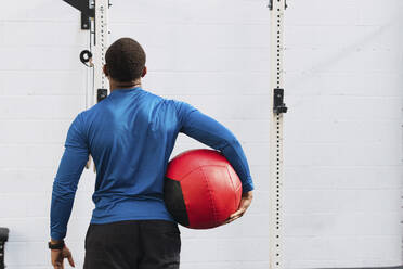 Sportler hält Medizinball vor einer Wand in der Turnhalle - PNAF02859