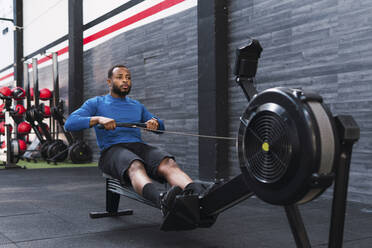 Athlete using rowing machine in gym - PNAF02880