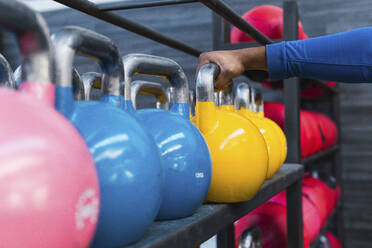 Hände eines Sportlers, der eine gelbe Kettlebell auf einem Regal im Fitnessstudio hält - PNAF02888