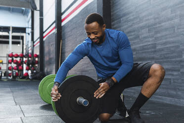 Lächelnder Athlet, der im Crossfit-Fitnessstudio Hantelscheiben in die Hantel steckt - PNAF02900