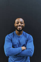 Smiling athlete with arms crossed against black background - PNAF02904