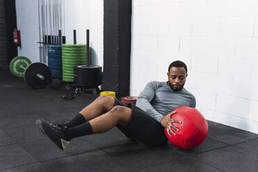 Sportler beim Training mit einem Medizinball auf dem Boden im Fitnessstudio - PNAF02915