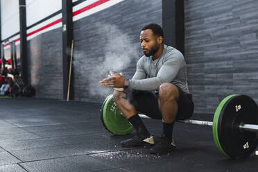 Sportler staubt Kreidepulver ab, das auf einer Langhantel im Fitnessstudio sitzt - PNAF02919