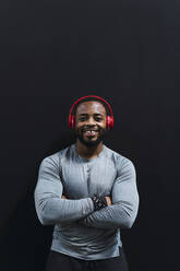 Smiling athlete with arms crossed standing against black background - PNAF02940