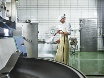Fleischer mit Schürze beim Waschen von Maschinen in einer Fabrik - CVF01862